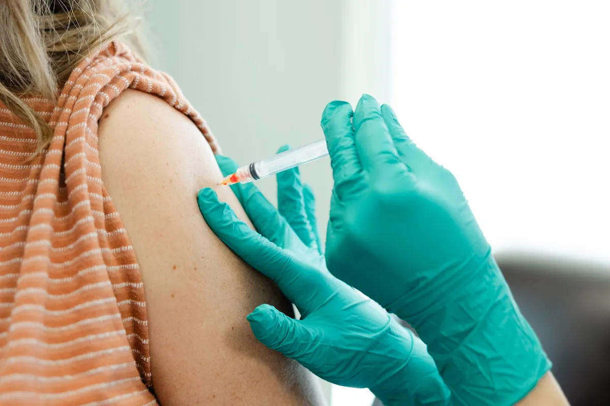 A gloved practitioner giving an intramuscular vitamin injection in a client’s upper arm