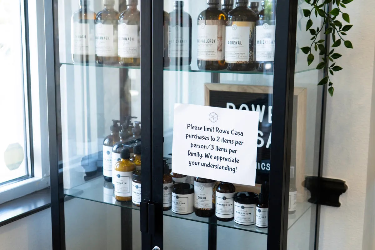 A glass-fronted cabinet of amber apothecary bottles, with a printed note asking customers to limit purchases to two items.