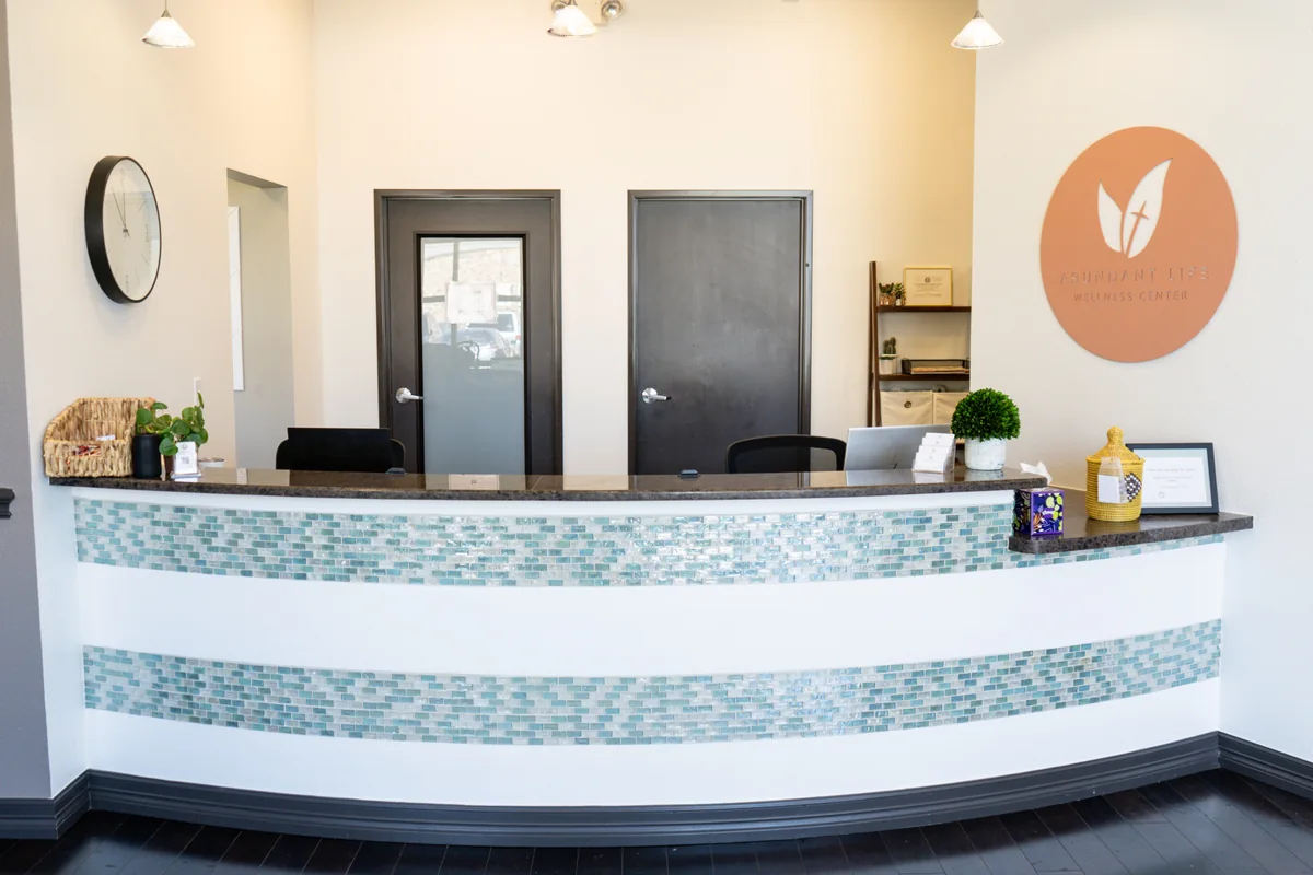 The practice reception desk with turquoise tile, plants, and the Abundant Life wall logo